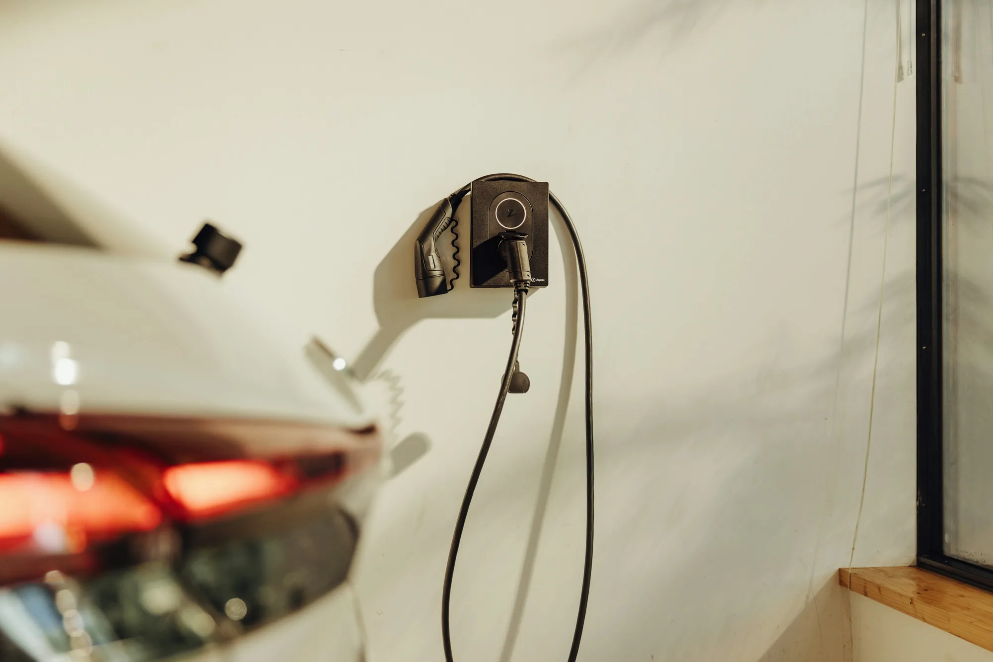 Wallbox an der Wand mit Ladekabel, im Vordergrund das Heck eines Elektroautos