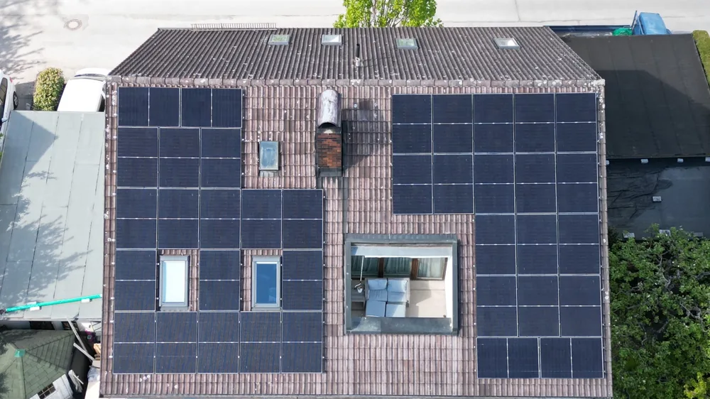 Mehrfamilienhaus von oben: Satteldach mit zwei Photovoltaik-Feldern rund um Dachfenster und Dachterrasse